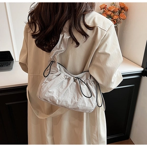 Dettaglio della borsa a tracolla in nylon a pieghe grigio chiaro con coulisse nere sul cappotto