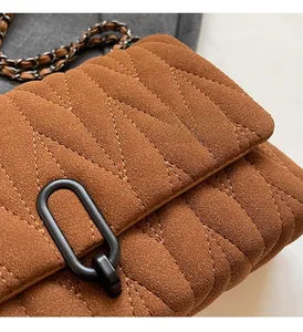 Close-up of brown suede crossbody bag featuring V-shaped quilting and metal chain strap