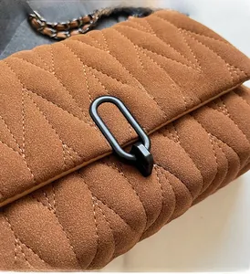 Detail of brown suede crossbody bag featuring V-shaped quilting and black oval metal lock