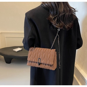 Detail of brown quilted suede shoulder bag featuring a metal chain strap and U-shaped clasp