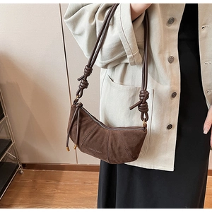 Détails d'un sac croissant en daim marron foncé avec un nœud en cuir élégant sur la bandoulière
