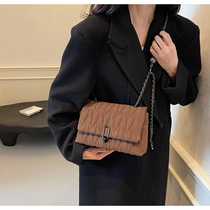 Brown quilted crossbody bag with metal chain shown on black coat in minimalist setting