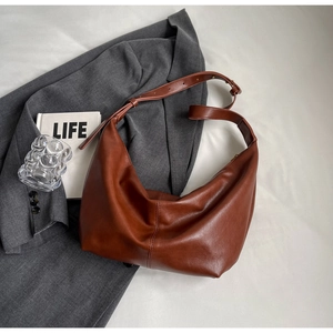 Brown leather crescent shoulder bag with vertical stitching and adjustable strap on a blazer
