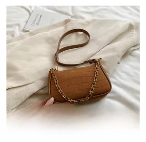 Brown crocodile texture baguette bag with golden chain detail on white fabric background