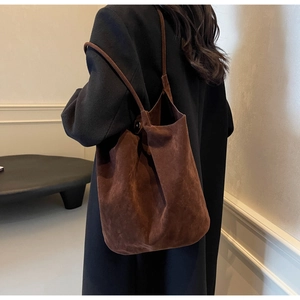 Brown suede bucket bag with fine shoulder strap worn by a model in soft interior light