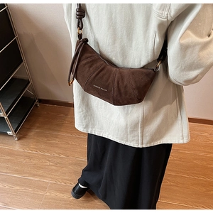 Détail du sac demi-lune en daim marron foncé avec plis élégants et logo argenté gravé