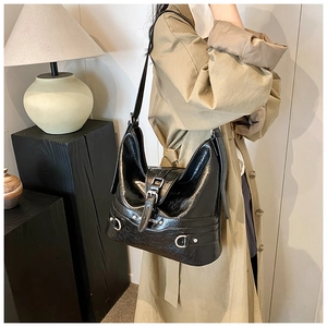 Close-up of black glossy PU leather shoulder bag with metallic buckle and stud details