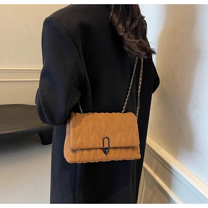 Brown suede crossbody bag with wave quilting and chic chain strap on a black coat