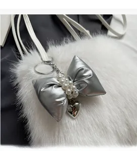 Detail of white faux fur bag featuring a silver bow charm with pearls and heart pendant
