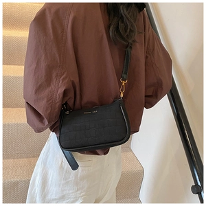 Detail of black crocodile texture shoulder bag with gold hardware and logo on strap