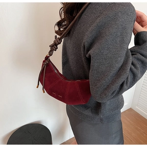 Détail du sac croissant en daim rouge avec bandoulière nouée et surpiqûres sur pull gris