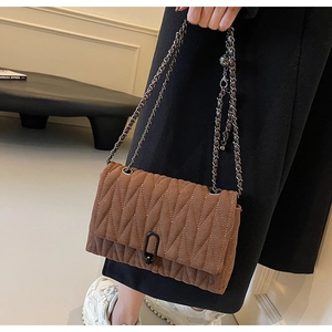 Detail of brown quilted crossbody bag featuring a matte metal clasp and woven chain strap