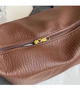 Gros plan sur la fermeture éclair dorée et le cuir marron grainé du sac fourre-tout