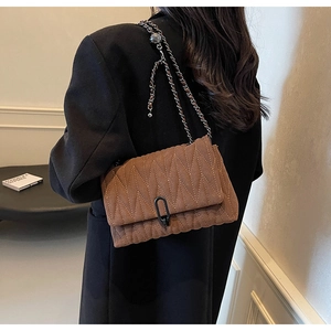 Detail of a brown quilted suede crossbody bag with wave texture and chain strap
