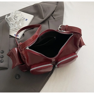 Detail view of dark red PU shoulder bag with multiple zippers on grey blazer background