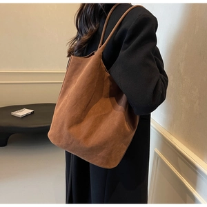 Detailed texture of caramel brown suede tote bag worn over a black classic coat