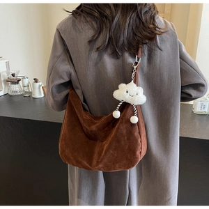 Detail of a brown suede hobo bag with a white plush cloud charm on a wide shoulder strap