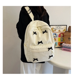 Détail du sac à dos en velours côtelé beige avec nœuds noirs et poche zippée avant