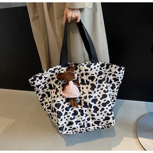 Detail of a large cow print tote bag with a cute mouse plush charm and black handles