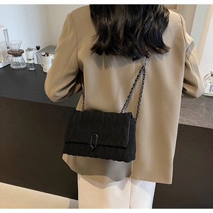 Detail view of a black quilted shoulder bag with wave stitching and metal chain strap on model
