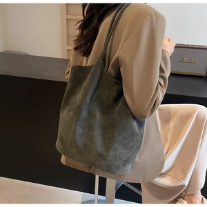 Detailed texture of dark grey-green suede leather tote bag shown in a lifestyle setting