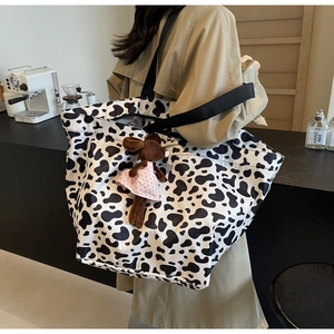 Detail view of a large canvas cow print tote bag with a plush toy on a model shoulder