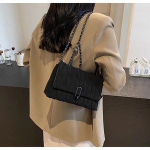 Detail of black quilted shoulder bag with V-shaped texture and gunmetal chain strap