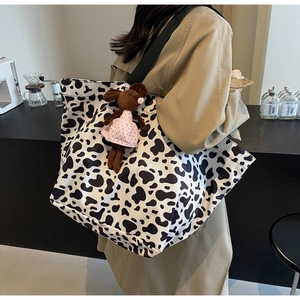 Close-up of a stylish cow print canvas tote bag with a cute plush mouse charm detail