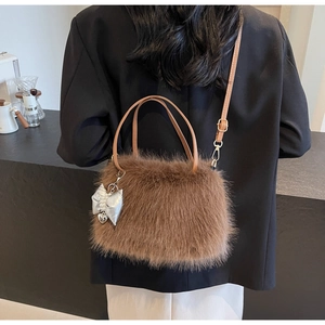 Detail view of brown plush crossbody bag with leather handles and silver bow charm