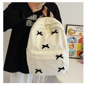 Détail d'un sac à dos blanc en velours côtelé avec nœuds noirs et poche latérale