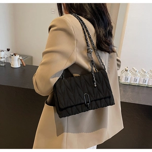 Detail of black quilted crossbody bag with metal chain strap and oval gunmetal lock