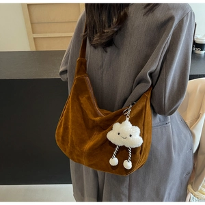 Detail view of brown suede hobo bag with a white cloud plush charm on a grey blazer