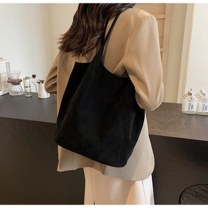 Detail of a black suede-textured tote bag shown on a model in a cozy cafe setting