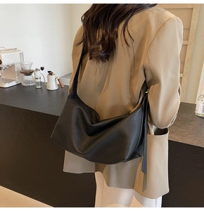 Détail du sac hobo souple noir à texture litchi porté par un mannequin en décor urbain