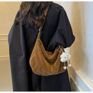 Brown suede shoulder bag with wide strap and cloud charm shown on model's shoulder