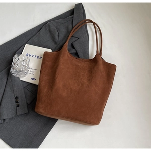 Minimalist brown suede tote bag with dual straps displayed on a stylish grey blazer suit