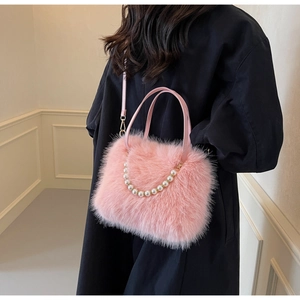 Detailed view of pink plush crossbody bag with pearl chain shown on model in black coat