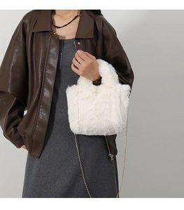 Close-up of white plush crossbody bag with a delicate gold chain strap on a model