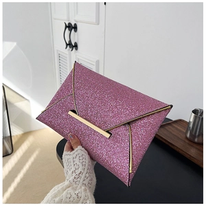 Gros plan d'une pochette enveloppe rose à paillettes avec bordure dorée par un mannequin