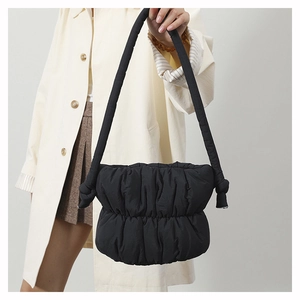 Close-up of black quilted puffer shoulder bag with stylish knotted strap detail on coat