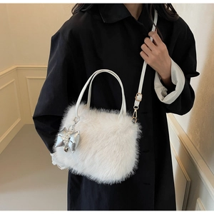 Close-up of white plush crossbody bag with pearl bow charm and leather straps