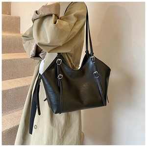 Detail of black faux leather tote bag with silver metal buckles on adjustable straps