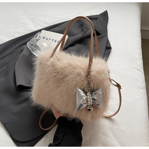 Beige plush crossbody bag with leather straps and a silver bow charm on a stylish table