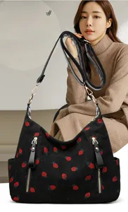 Detail of black corduroy shoulder bag featuring red strawberry patterns and gold hardware