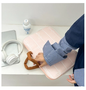 Detailed view of pink fabric laptop bag with white bow pattern and brown padded handles