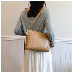 Detail of hand-woven camel PU leather shoulder bag with metallic ball charm on a model