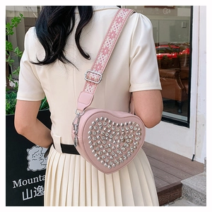 Détail du sac à main rose en forme de cœur avec rivets argentés et bandoulière brodée