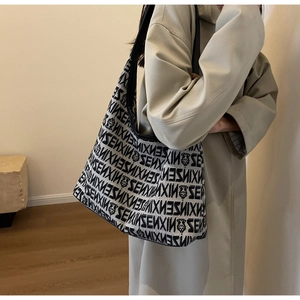Detail showing the monogram pattern and black leather strap on a large canvas tote bag
