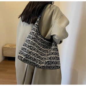 Detail of a large knit tote bag with SENXIN jacquard pattern worn over a trench coat