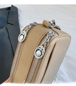 Detailed close-up of smooth double metal zippers on a beige leather camera crossbody bag